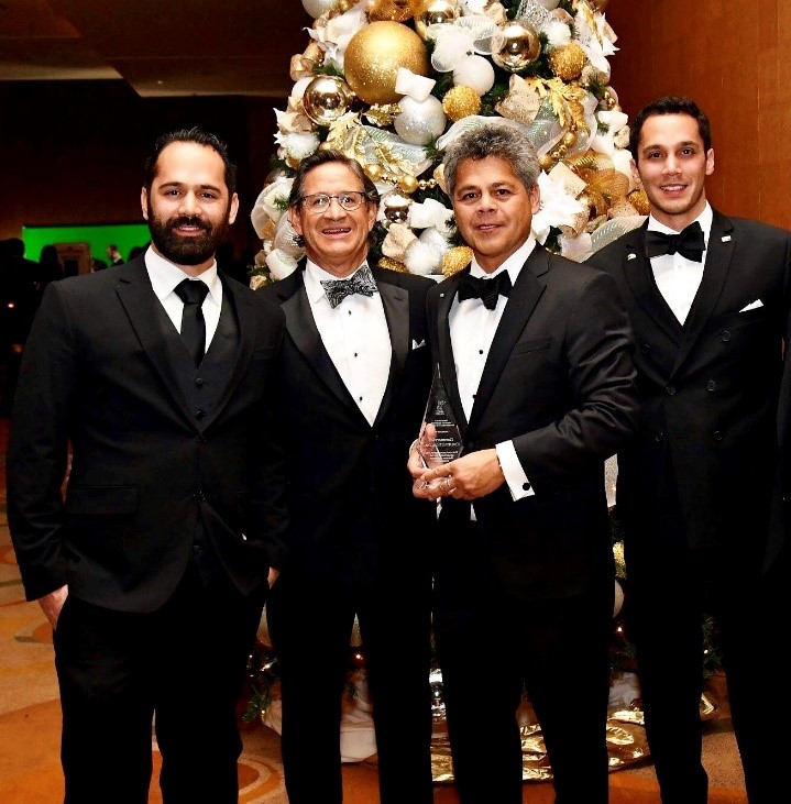 CCI Industrial Constructors - Four men in formal black tuxedos gathered at an elegant event, standing before an ornate, festive decoration.