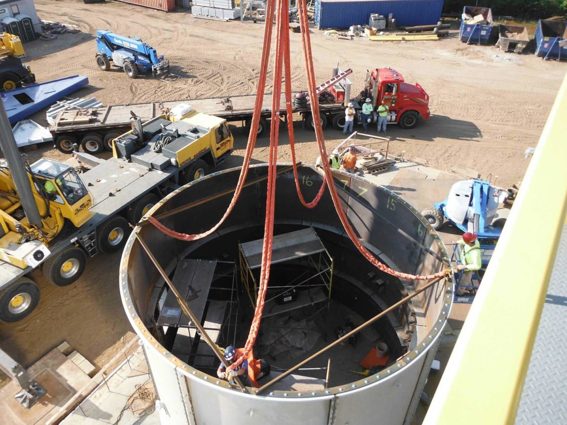 CCI employee standing on scaffolding and securing rigging to a large metal cylinder