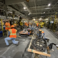CCI Industrial Constructors - Workers in high-visibility vests and hard hats operating machinery on a busy factory floor during a manufacturing process.