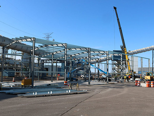 CCI Industrial Constructors - Construction activity at an industrial site, with steel structures being erected and a crane in operation under a clear blue sky.