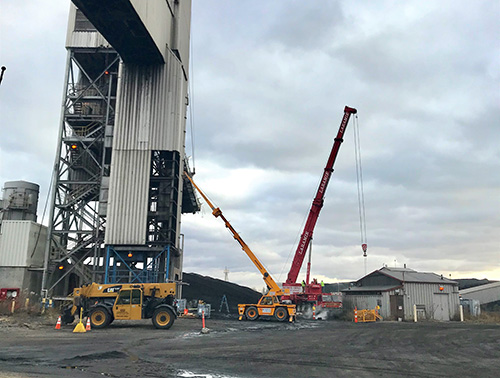 CCI Industrial Constructors - Industrial teamwork: a telehandler and a large mobile crane work in concert at an industrial site, against a backdrop of metal structures and heavy-duty machinery.