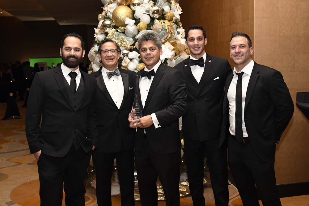 CCI Industrial Constructors - Group of five men dressed in formal attire with tuxedos, posing together at an event, with one holding an award and a decorated christmas tree in the background.