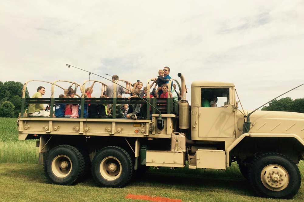 CCI Industrial Constructors - A group of people enjoying a ride in the back of a military-style truck on a green field.