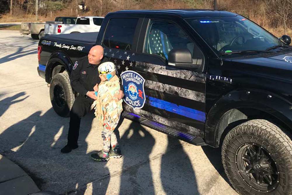CCI Industrial Constructors - A police officer kneeling down to engage with a child dressed in a colorful outfit next to a police vehicle with a distinctive black and blue design.