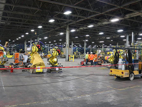 CCI Industrial Constructors - A busy factory floor with industrial robots and workers engaged in manufacturing activities, showcasing a blend of automation and human labor.