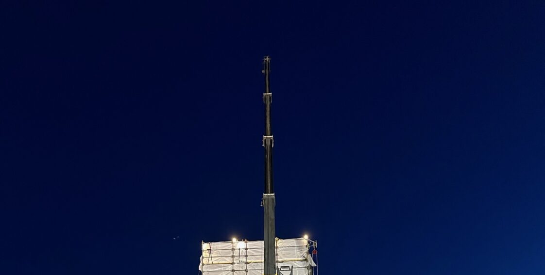 CCI Industrial Constructors - A towering mobile crane at a construction site during the evening, illuminated by artificial lighting, with a large, covered structure in the background.