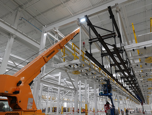 CCI Industrial Constructors - Installation of industrial equipment in a modern manufacturing facility with workers operating a cherry picker to reach the ceiling-mounted machinery.