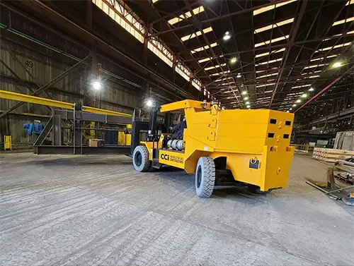 CCI Industrial Constructors - An industrial forklift transporting a large yellow container inside a warehouse.