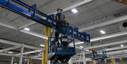 CCI Industrial Constructors - A worker operating a blue scissor lift for maintenance or inspection tasks in an industrial facility with overhead structures.