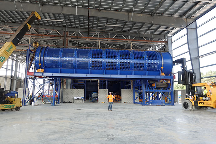 CCI Industrial Constructors - A large blue industrial machine being installed inside a spacious warehouse, with a worker overseeing the process and various lifting equipment in the vicinity.