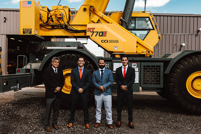CCI Industrial Constructors - Four professionals in suits standing confidently in front of a large yellow mobile crane at an industrial facility.