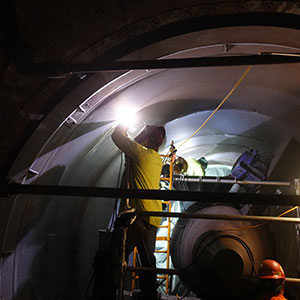 Man in a yellow shirt welding inside a large metal pipe