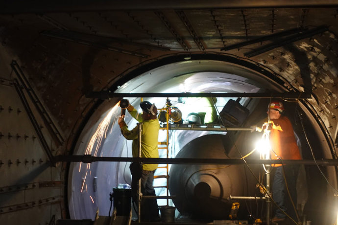 CCI Industrial Constructors - Workers conducting maintenance or inspection inside a large industrial pipe or tunnel, illuminated by work lights.