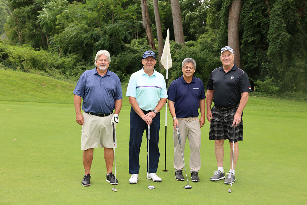 CCI Industrial Constructors - Four smiling golfers posing with a golf flag on a green course.