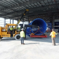 CCI Industrial Constructors - Workers on a construction site maneuvering heavy industrial equipment with the assistance of a forklift inside a spacious warehouse.