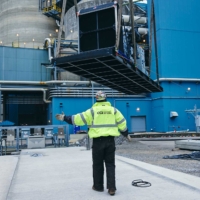 CCI Industrial Constructors - A construction worker in a high-visibility vest and hard hat gestures on a site dotted with industrial equipment and structures.
