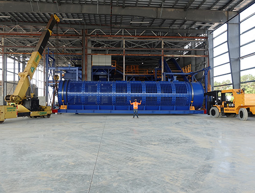 CCI Industrial Constructors - A worker supervising the installation of a large blue industrial machine with a telescopic handler inside a factory building.
