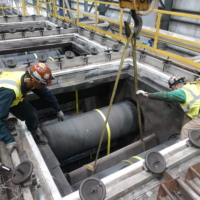 CCI Industrial Constructors - Workers in safety gear carefully maneuver a large cylindrical object into place at an industrial site.