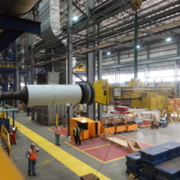 CCI Industrial Constructors - A spacious industrial facility with a large yellow crane lifting heavy machinery, workers in safety gear overseeing the operation, and an array of equipment and tools organized throughout the workspace.