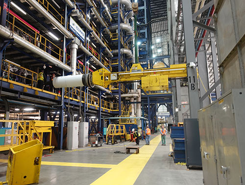 CCI Industrial Constructors - Industrial maintenance symphony: inside a complex manufacturing facility, where a powerful overhead crane effortlessly moves heavy machinery above workers navigating the metallic maze.