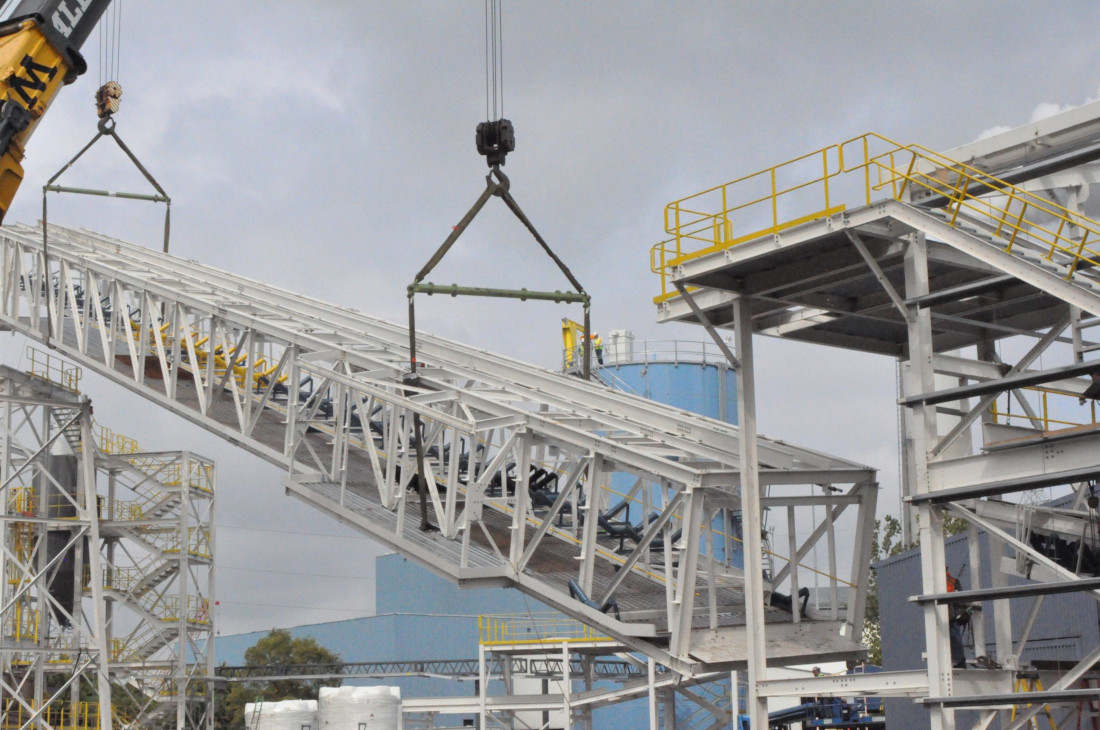 CCI Industrial Constructors - Industrial lifting in action: a crane hoists a heavy conveyor section into place at a construction or processing plant site, showcasing the synergy between engineering and construction.