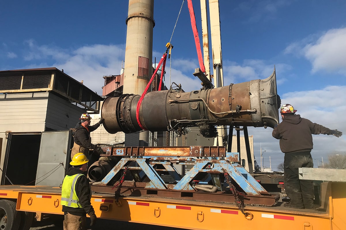 CCI Industrial Constructors - Workers in hard hats overseeing the loading of a large industrial component onto a truck at an industrial maintenance power plant facility.