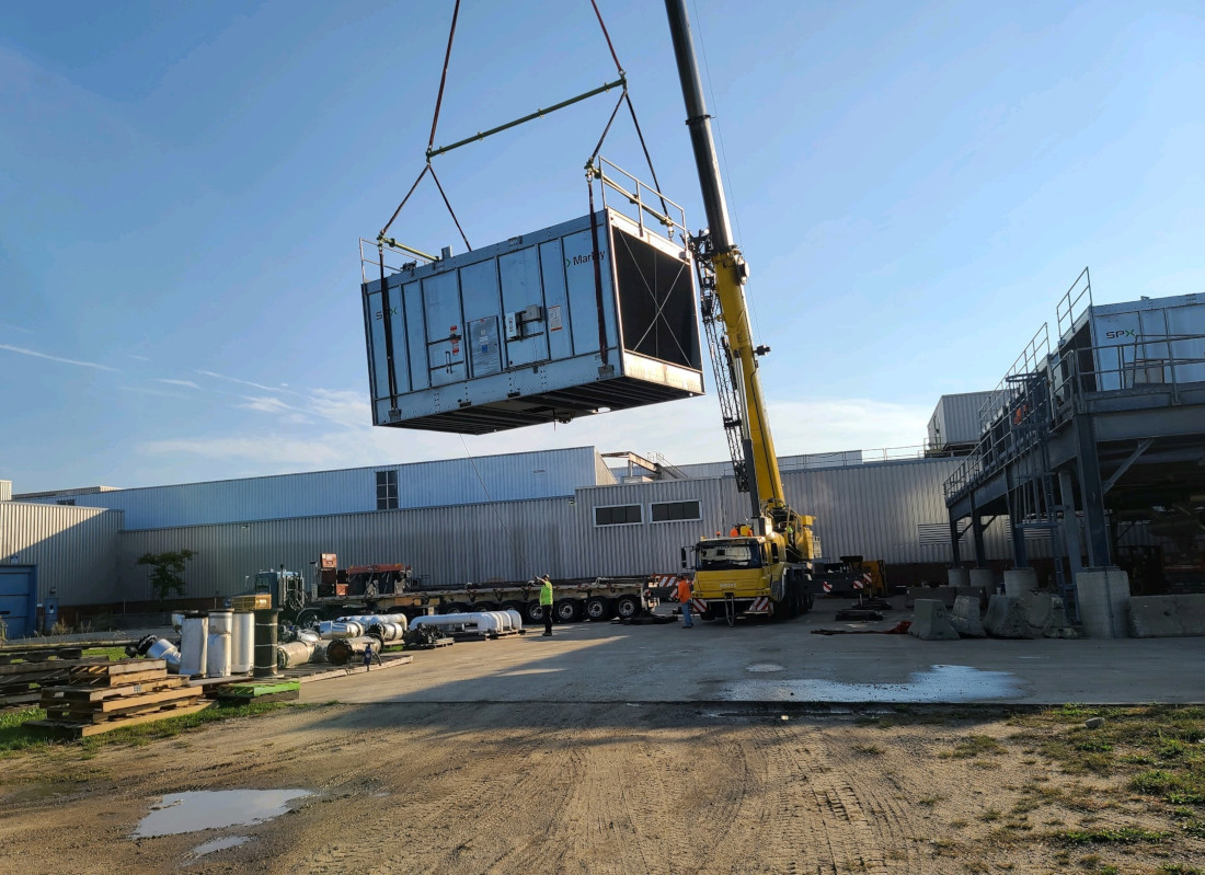 CCI Industrial Constructors - A large industrial crane hoisting a modular container next to a warehouse under a clear blue sky.