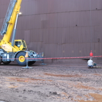 CCI Industrial Constructors - A mobile crane at an industrial site with workers engaged in what appears to be a safety or measurement operation on the ground.