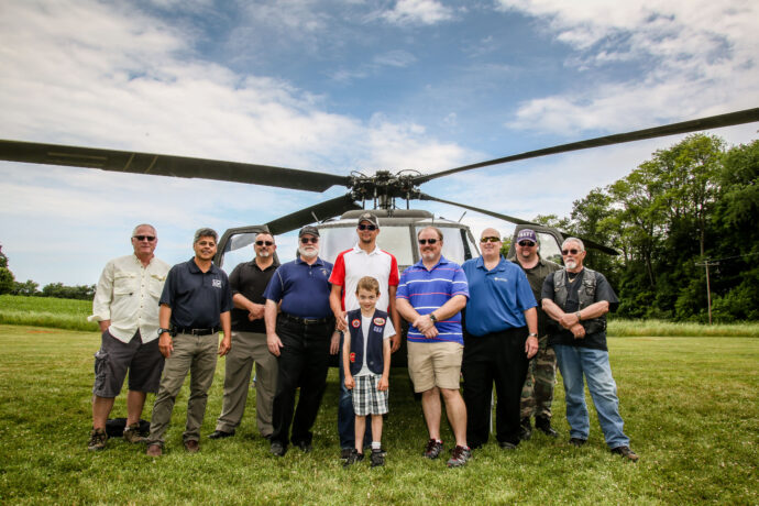 CCI Industrial Constructors - Group of individuals posing confidently in front of a helicopter on a grassy field, with a clear sky overhead; a sense of camaraderie and pride evident in their stance.