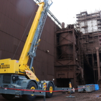 CCI Industrial Constructors - An industrial crane parked outside a large factory building, likely engaged in construction or maintenance work.