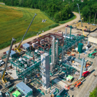 CCI Industrial Constructors - Aerial view of an industrial construction site with a scaffold-clad structure, heavy machinery, and workers amidst a lush green landscape.