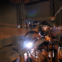 CCI Industrial Constructors - A skilled welder focused on his work, the bright arc of the welding torch illuminating the intense concentration in a dimly lit workshop.