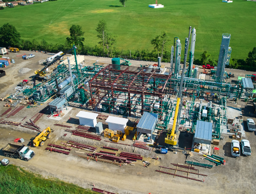 CCI Industrial Constructors - Aerial view of an industrial facility with complex piping and structures, surrounded by green fields, with construction and transportation equipment scattered around the site.