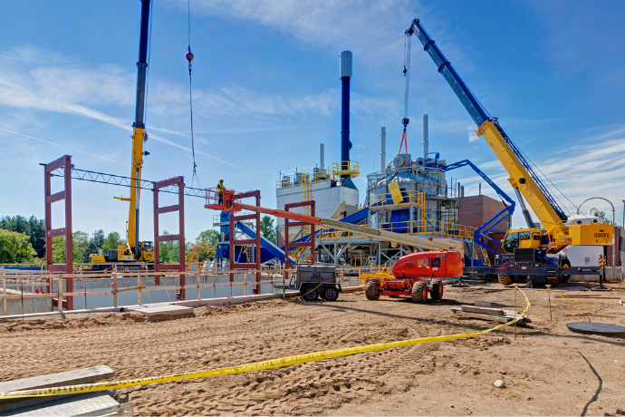 CCI Industrial Constructors - Construction site in action with cranes and heavy machinery installing large steel structures on a bright sunny day.