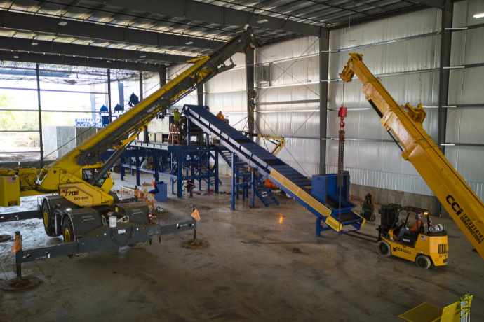 CCI Industrial Constructors - Industrial setting with heavy machinery including a yellow mobile crane, conveyor systems, and a forklift, all within a spacious warehouse environment.