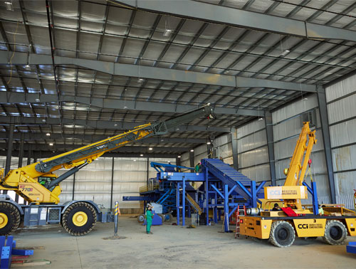 CCI Industrial Constructors - Industrial setting with a telehandler and a mobile crane operating near a tall steel structure, depicting a scene of active heavy machinery work inside a spacious warehouse.